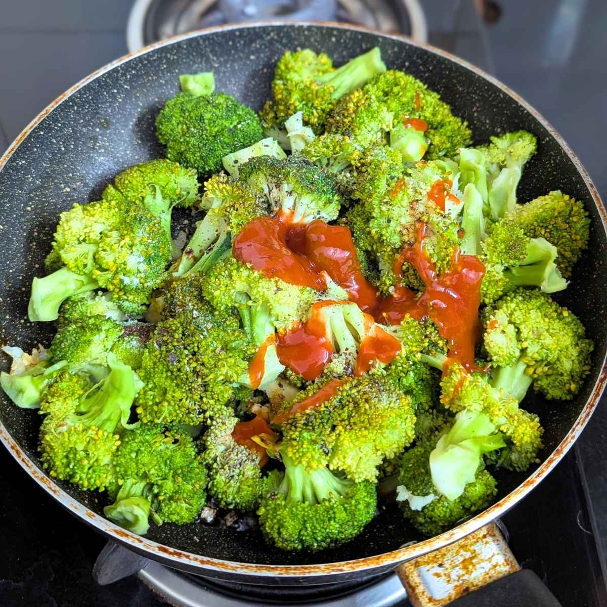 Broccoli florets in a pan with red chili sauce